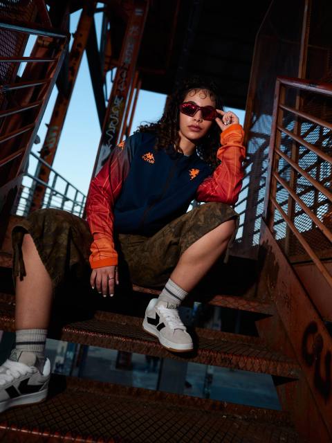 A model poses on metal steps wearing the Genoa CFC x Kappa FuturFestival pre-match jacket.