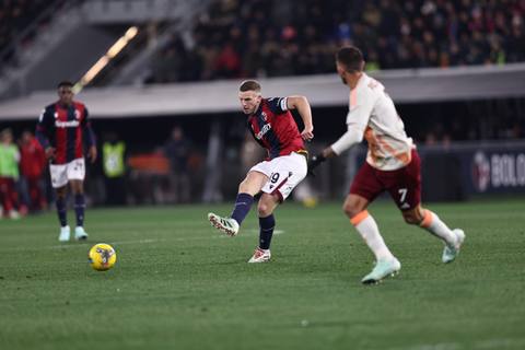 Lewis Ferguson of Bologna FC kicks the ball during a match, wearing the club's red and blue home shirt.