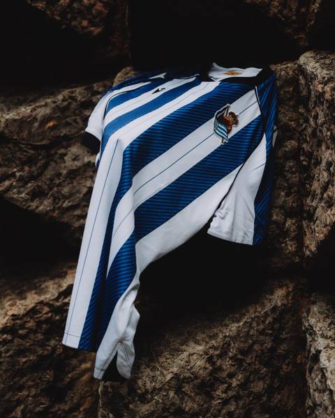 The Real Sociedad 2025/26 home shirt displayed on a rocky surface.