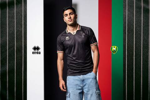 A model presents the ADO Den Haag 2025/26 away football shirt, featuring a dark pinstripe design with a retro collar in red, green and gold.