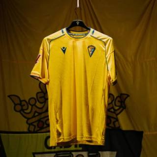 The yellow Cádiz CF home shirt hanging against a matching club flag.
