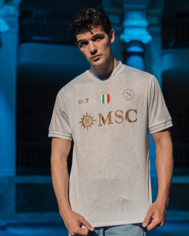 A model wearing the SSC Napoli 2025/26 away shirt by EA7, featuring a white base with gold details and a subtle sublimated pattern.