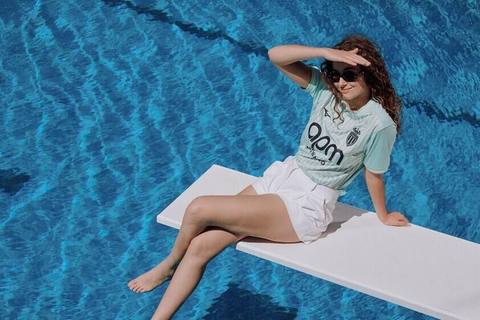 A model wears the AS Monaco light blue third shirt while posing on a diving board over a swimming pool.