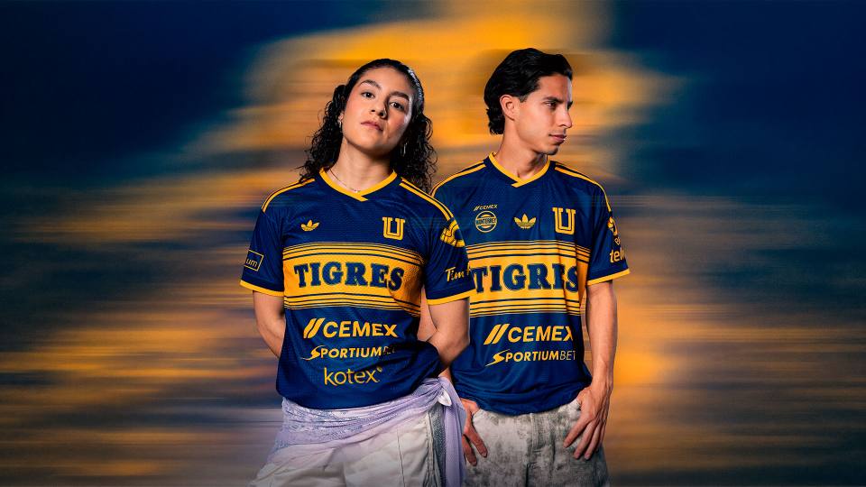 Two models showcasing the new Tigres UANL away shirt in blue with a yellow chest stripe.