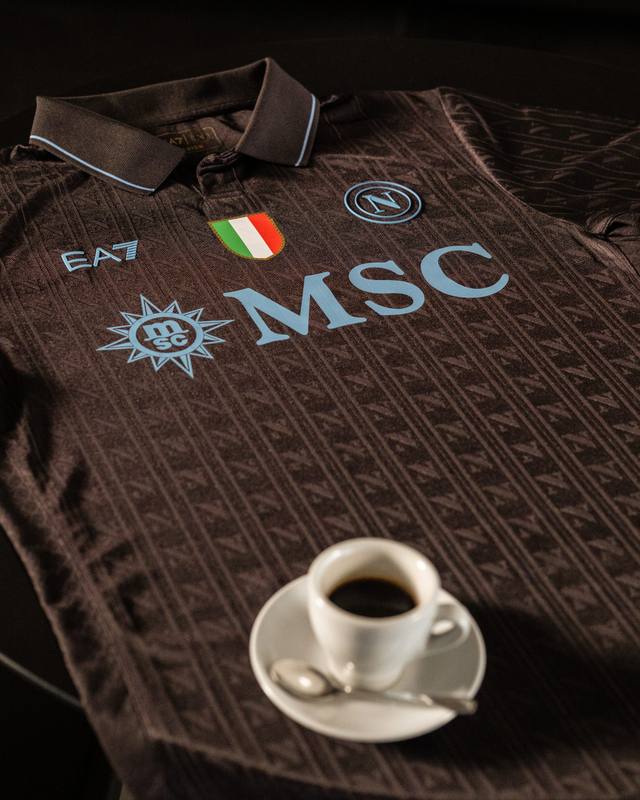 A promotional close-up of the SSC Napoli 2025/26 coffee-themed third shirt, featuring a brown textured design with light blue accents, displayed next to a cup of espresso.