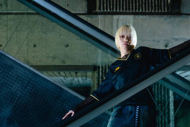 A model wears the black and gold Genoa CFC third shirt in a promotional campaign photoshoot on an escalator.