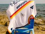 The U.S. Lecce away shirt is draped upside down over a blue chair on a rocky beach.