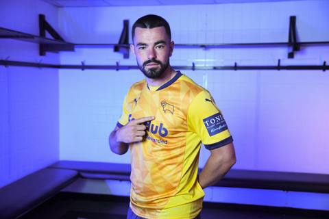A male player posing in the yellow Derby County 2024/25 third shirt with a geometric front panel pattern.