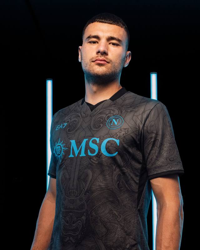 A model wears the SSC Napoli 2024/25 third shirt, which features a detailed dark grey graphic pattern and bright blue details.