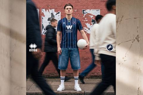 A model presents the Millwall FC home shirt for the 2026/27 season, featuring a navy blue design with white vertical pinstripes.