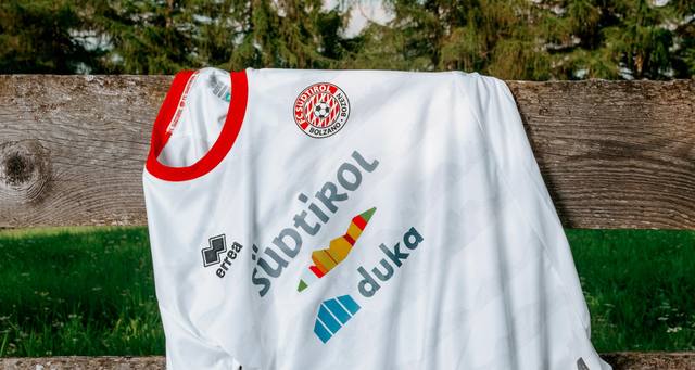 The FC Südtirol 2024/25 home shirt draped over a wooden fence in an outdoor setting.