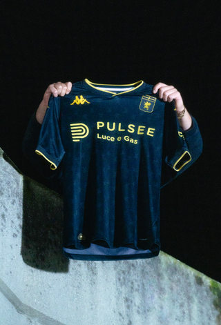 The Genoa CFC 2024/25 third shirt, featuring a dark base with yellow logos, held up against a dark night sky.