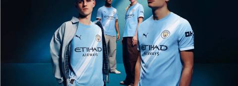 Manchester City players wear the 2025/26 home shirt featuring a diagonal white sash design.