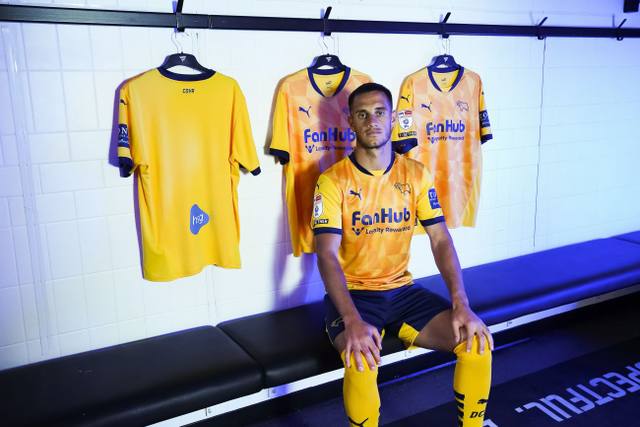 Derby County player models the gold 2024/25 third kit in a dressing room setting.