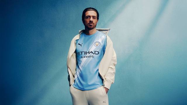 Jack Grealish models the Manchester City 2025/26 home shirt featuring a white diagonal sash.