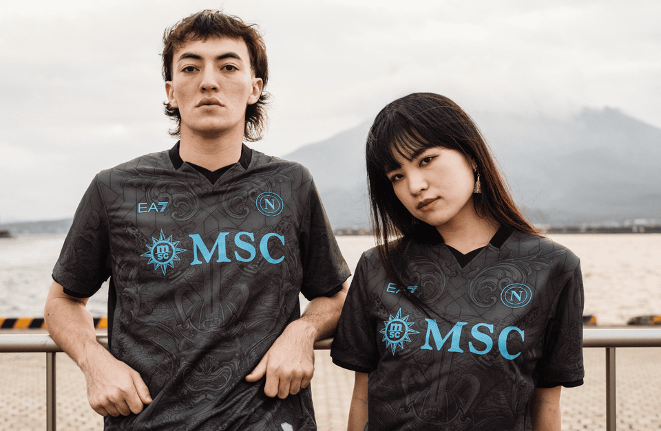 Two models posing in the SSC Napoli 2024/25 third shirt, which features a dark grey patterned base with light blue branding.