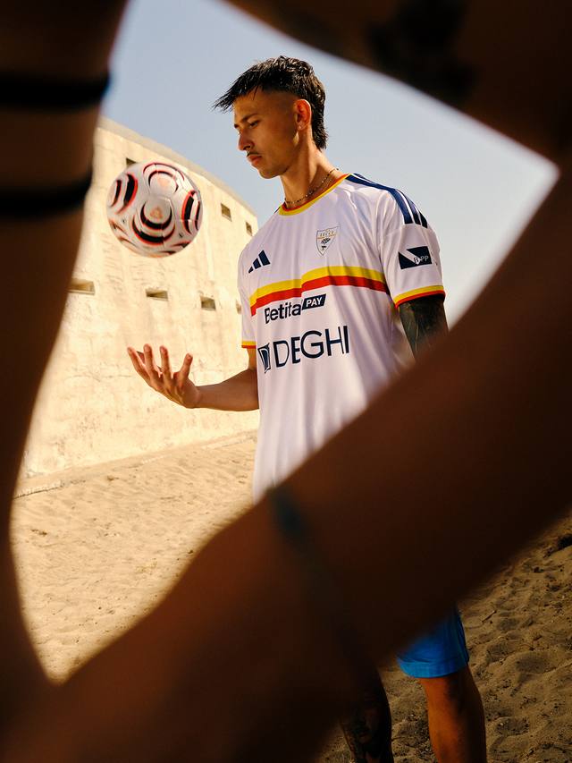 A player models the U.S. Lecce away shirt on a beach, framed by a foreground element.