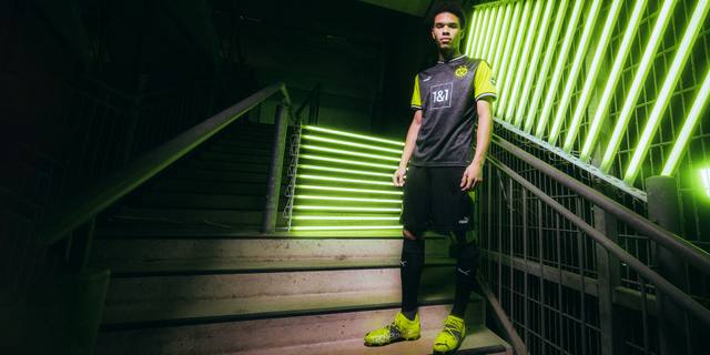A model poses on illuminated stairs wearing the Borussia Dortmund 2020/21 special edition retro kit.